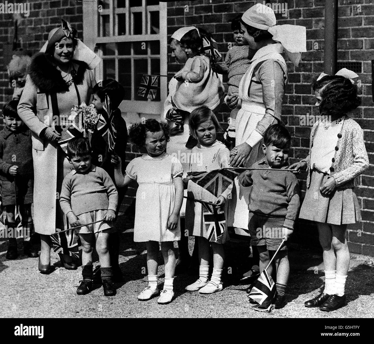 La regina (ora la regina madre) che si posa con i piccoli tot alla casa della regina Mary per i bambini durante il giro reale di Aldershot, Hampshire. Foto Stock