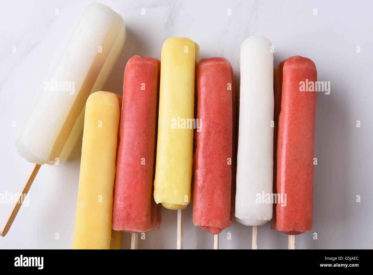 Vista dall'alto di un gruppo di assortiti pop di ghiaccio su un bancone di marmo alto. Rosso, giallo e bianco aromatizzate alla frutta pop sui loro lati. Foto Stock