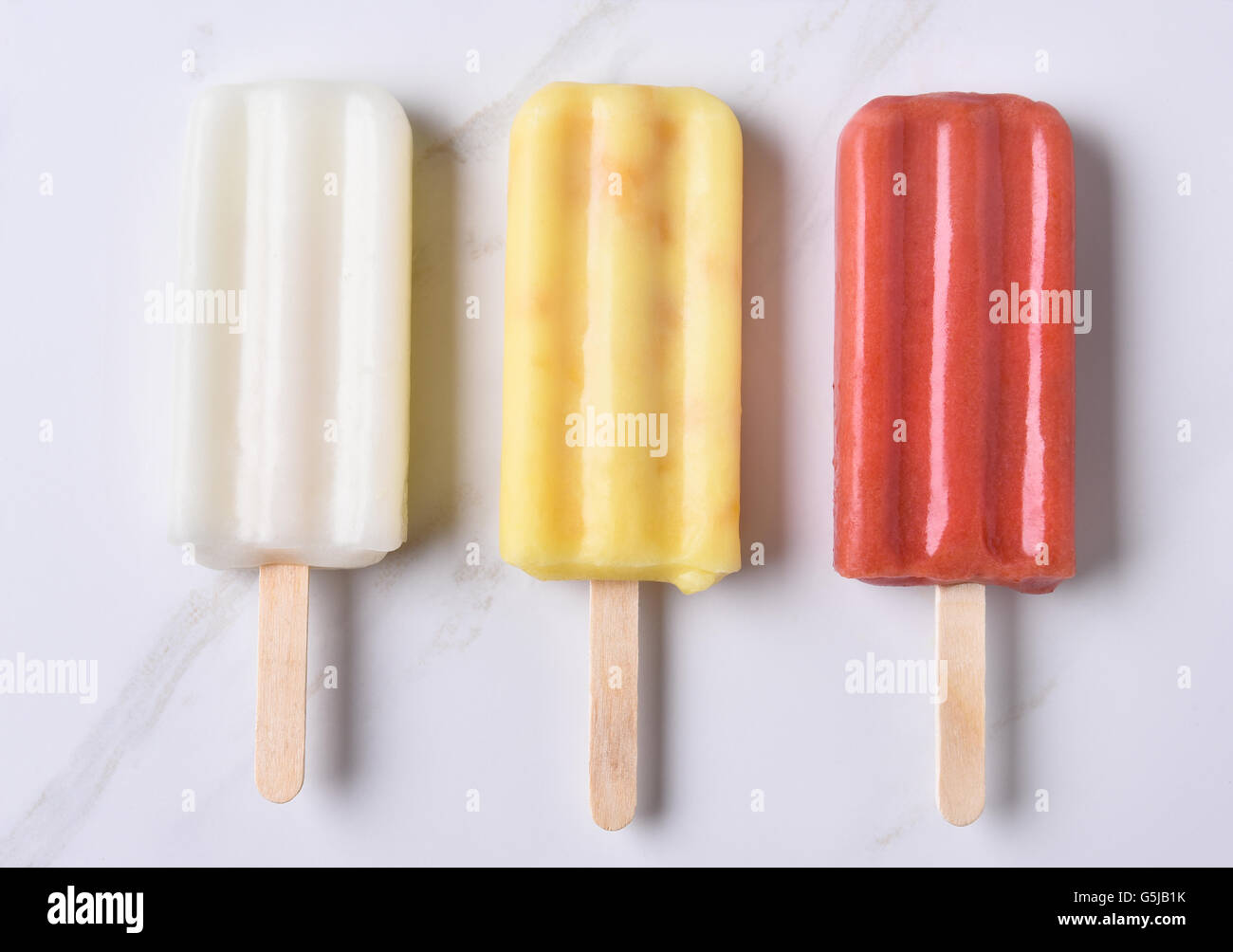 Vista superiore di tre diverse pop di ghiaccio su un bancone di marmo alto. Rosso, giallo e bianco aromatizzate alla frutta pop. Foto Stock