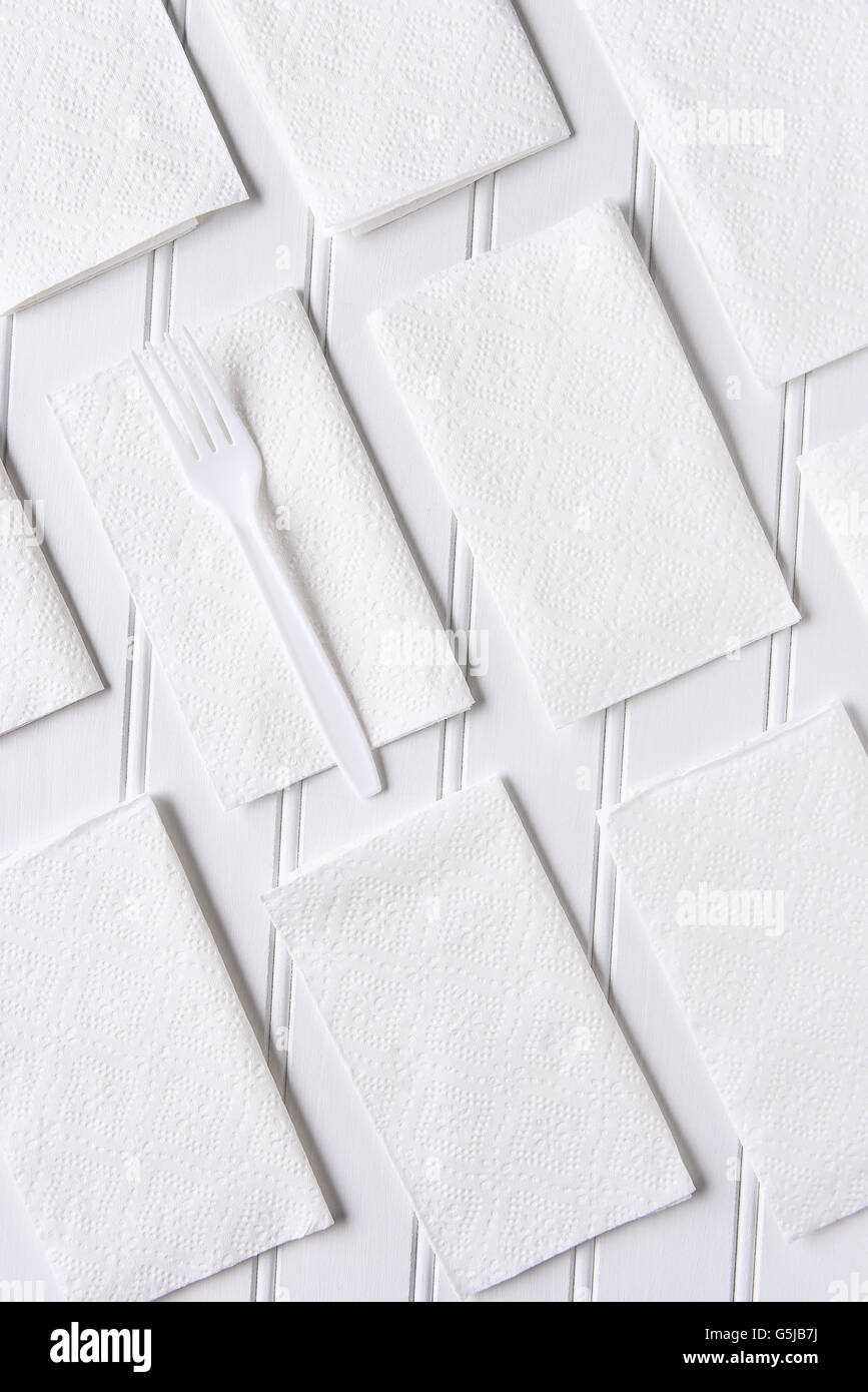 Tovaglioli bianchi su un tavolo bianco. Una singola forcella di plastica su un tovagliolo. Formato verticale a partire da un angolo di alta. Foto Stock