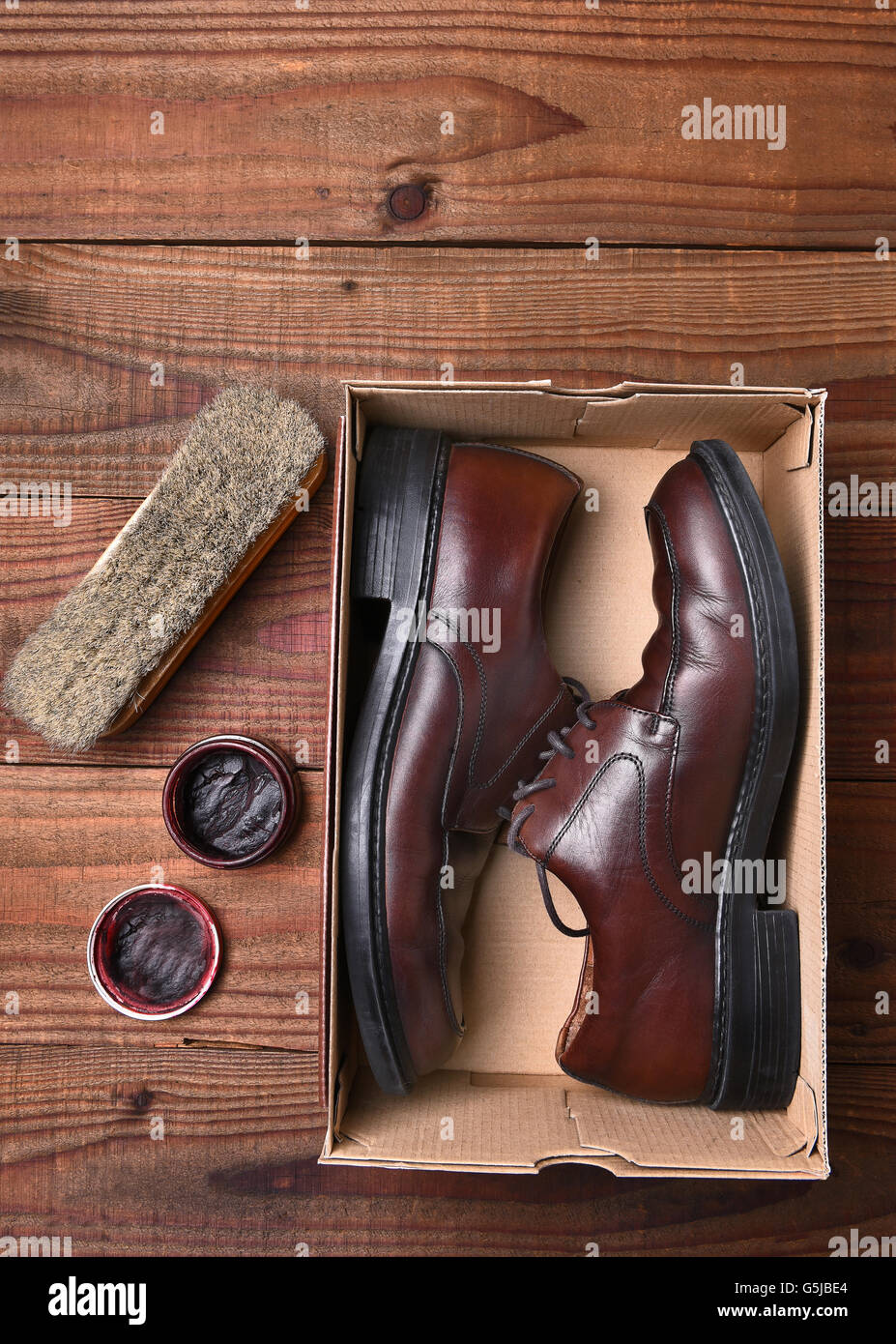 Un paio di scarpe in una scatola di scarpe con il polacco e il pennello su un pavimento in legno scuro. Formato verticale con copyspace, visto formano un angolo di alta. Foto Stock