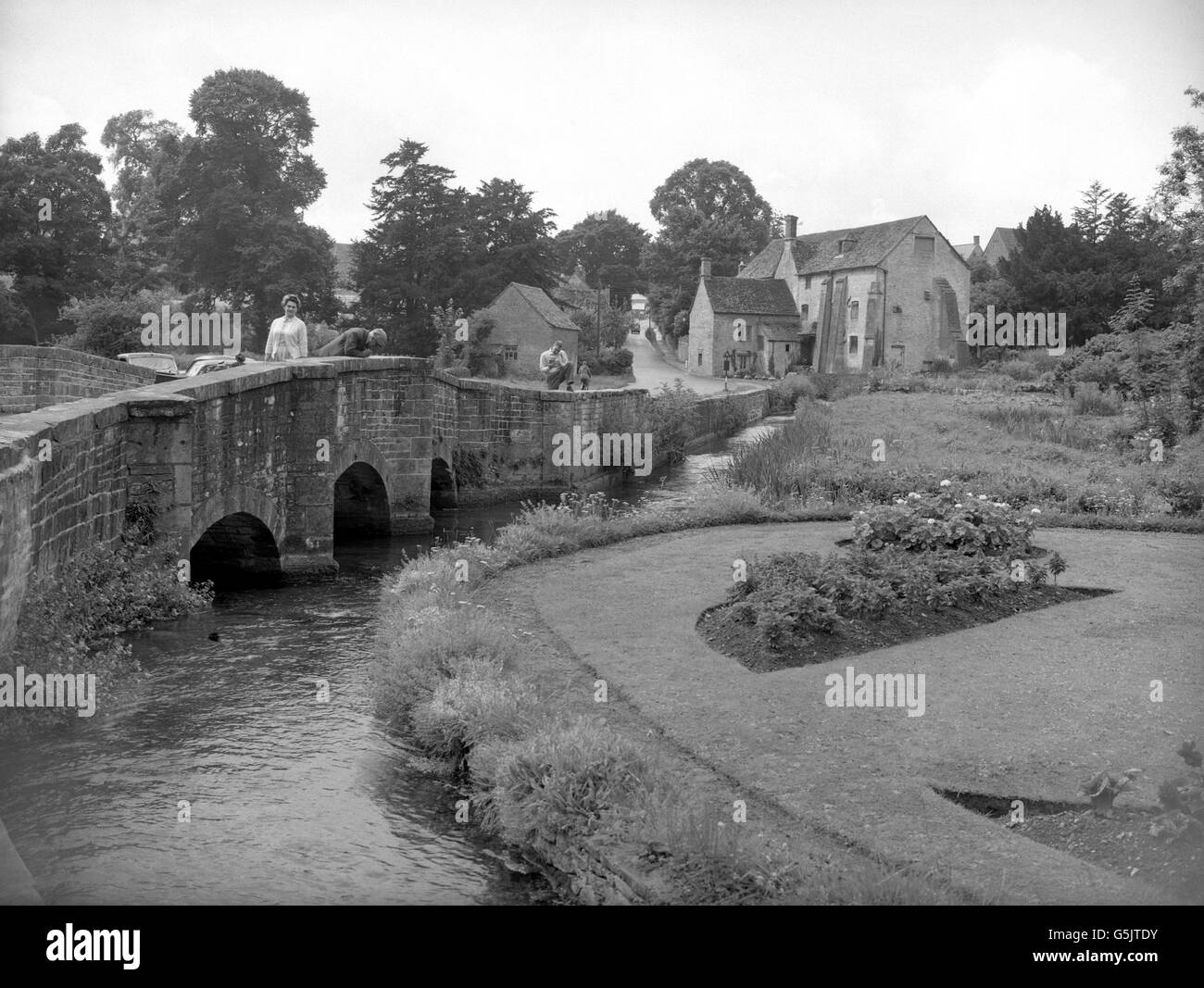 Una vista di un ponte che attraversa il fiume Colne a Bibury, Gloucestershire. Sullo sfondo è una vecchia casa mulino, con la strada che conduce a Cirencester. Foto Stock