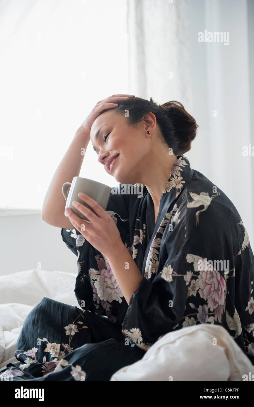Donna di bere caffè sul letto Foto Stock