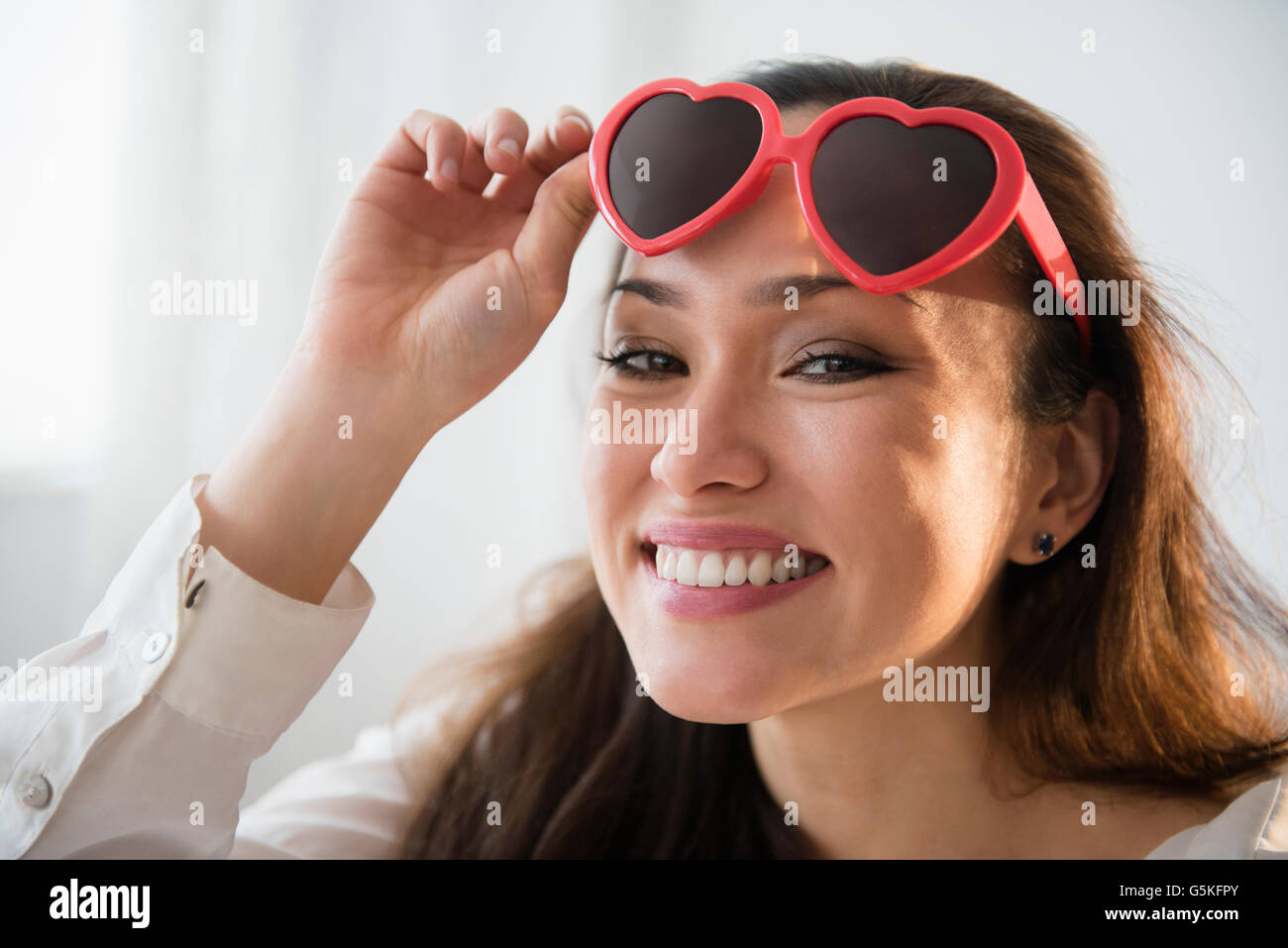 Donna sorridente indossando a forma di cuore ad occhiali da sole Foto Stock