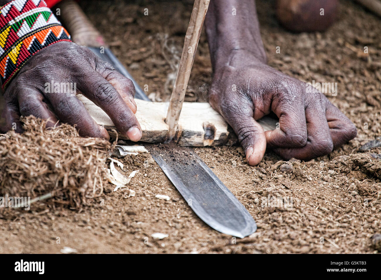 Giovane guerriero Masai inizia un incendio con bastoni e un coltello nel villaggio dei masai in Kenya, Africa. Foto Stock