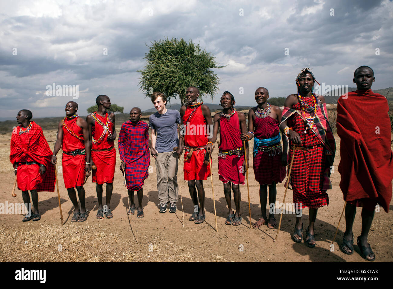 Un gruppo di guerrieri Masai e un turista facendo un cerimoniale di danza in un villaggio Masai, Kenya, Africa. Foto Stock