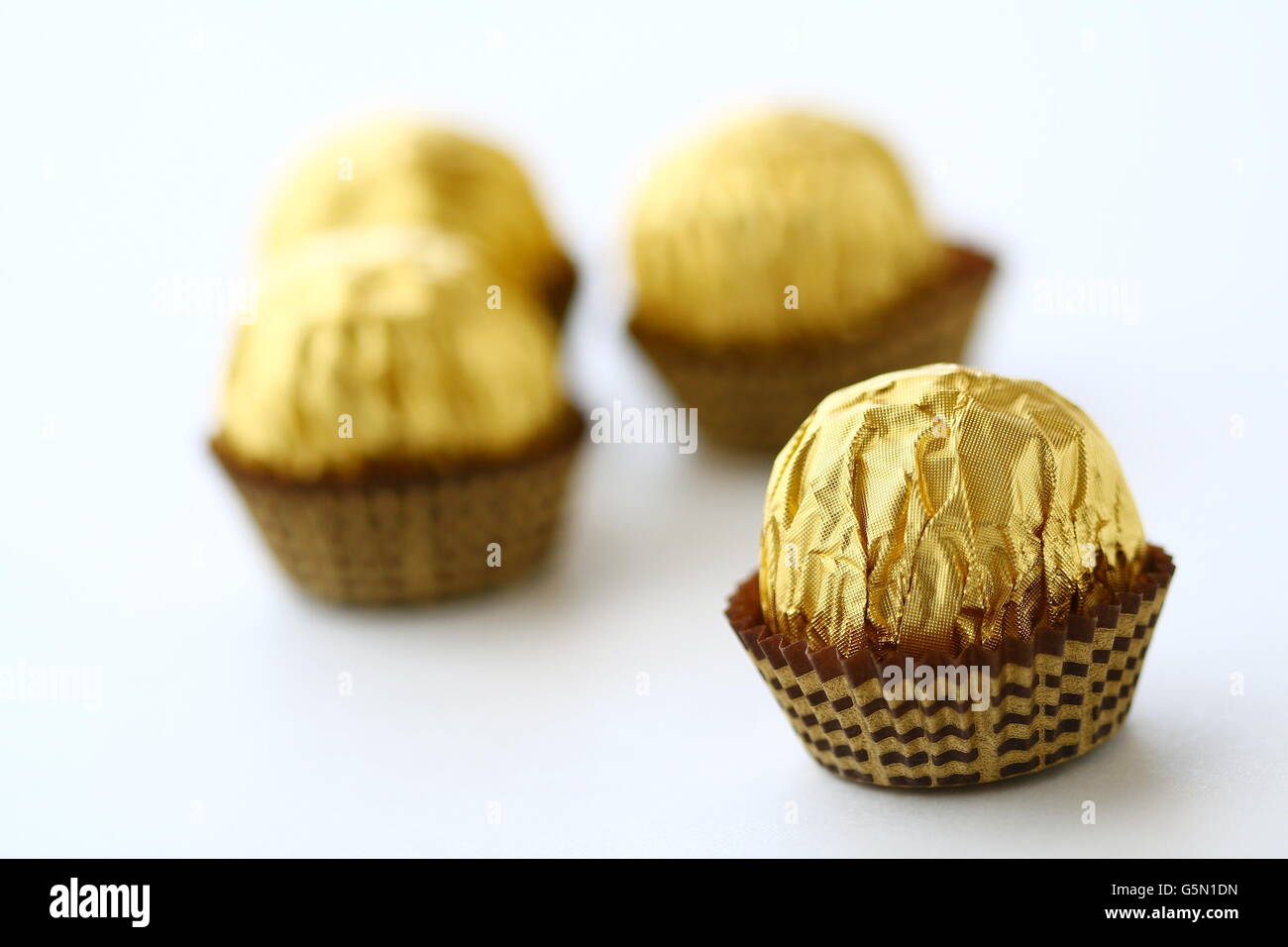 Close up di cioccolatini incartati singolarmente in oro involucro metallico contro uno sfondo bianco Foto Stock