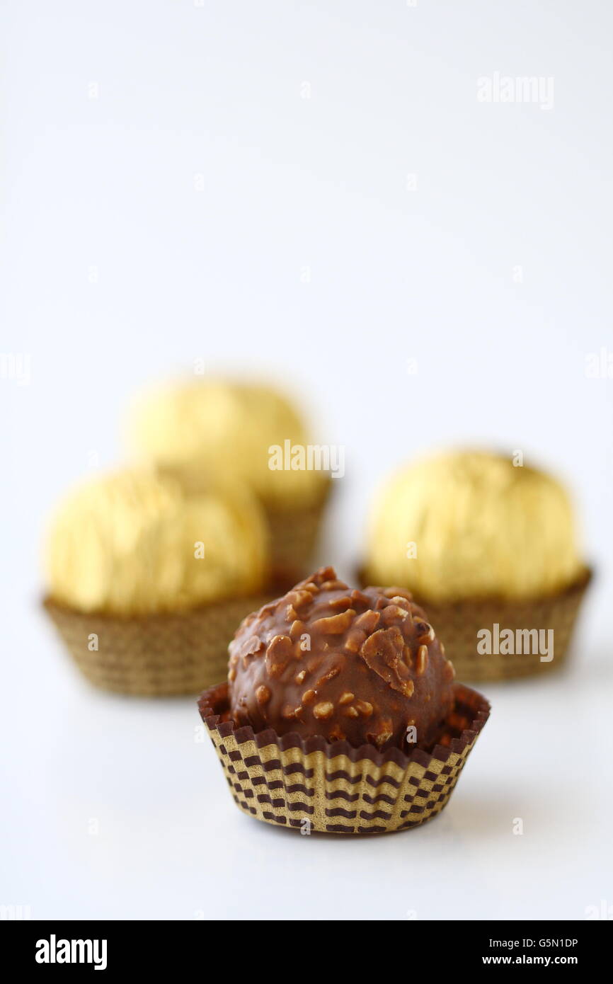 Close up di cioccolatini incartati singolarmente in oro involucro metallico contro uno sfondo bianco Foto Stock
