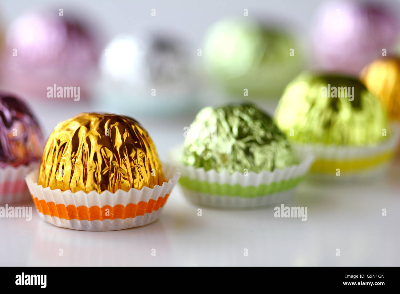 Close up di cioccolatini incartati singolarmente in involucro metallico contro uno sfondo bianco Foto Stock