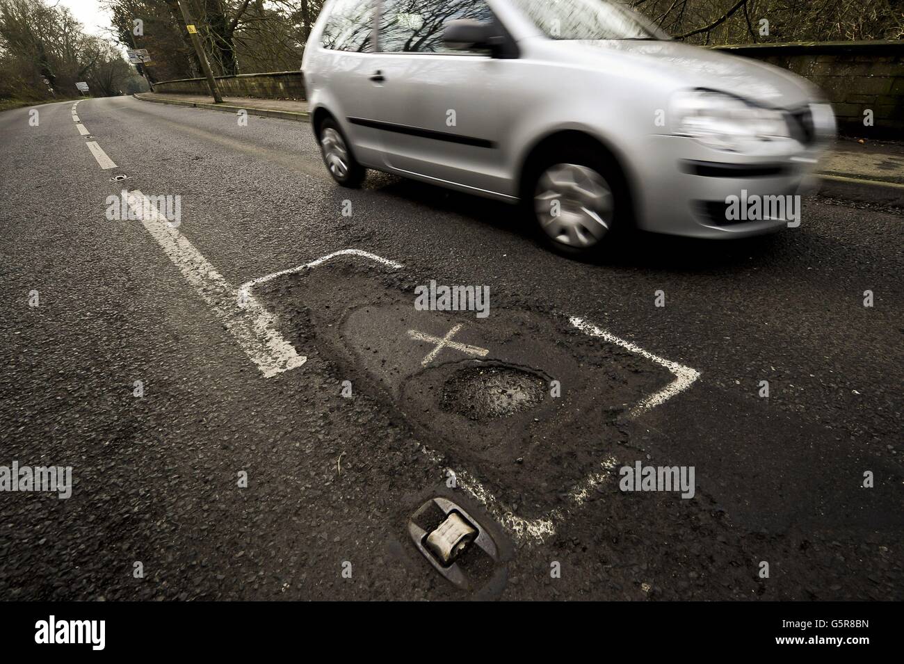 Le automobili passano una strada pesantemente pottolata in Gloucestershire come molte strade nel sud-ovest hanno bisogno di lavori di riparazione e di ripavimentazione dopo un anno di piogge pesanti e recenti inondazioni, creando buche e detriti. Foto Stock