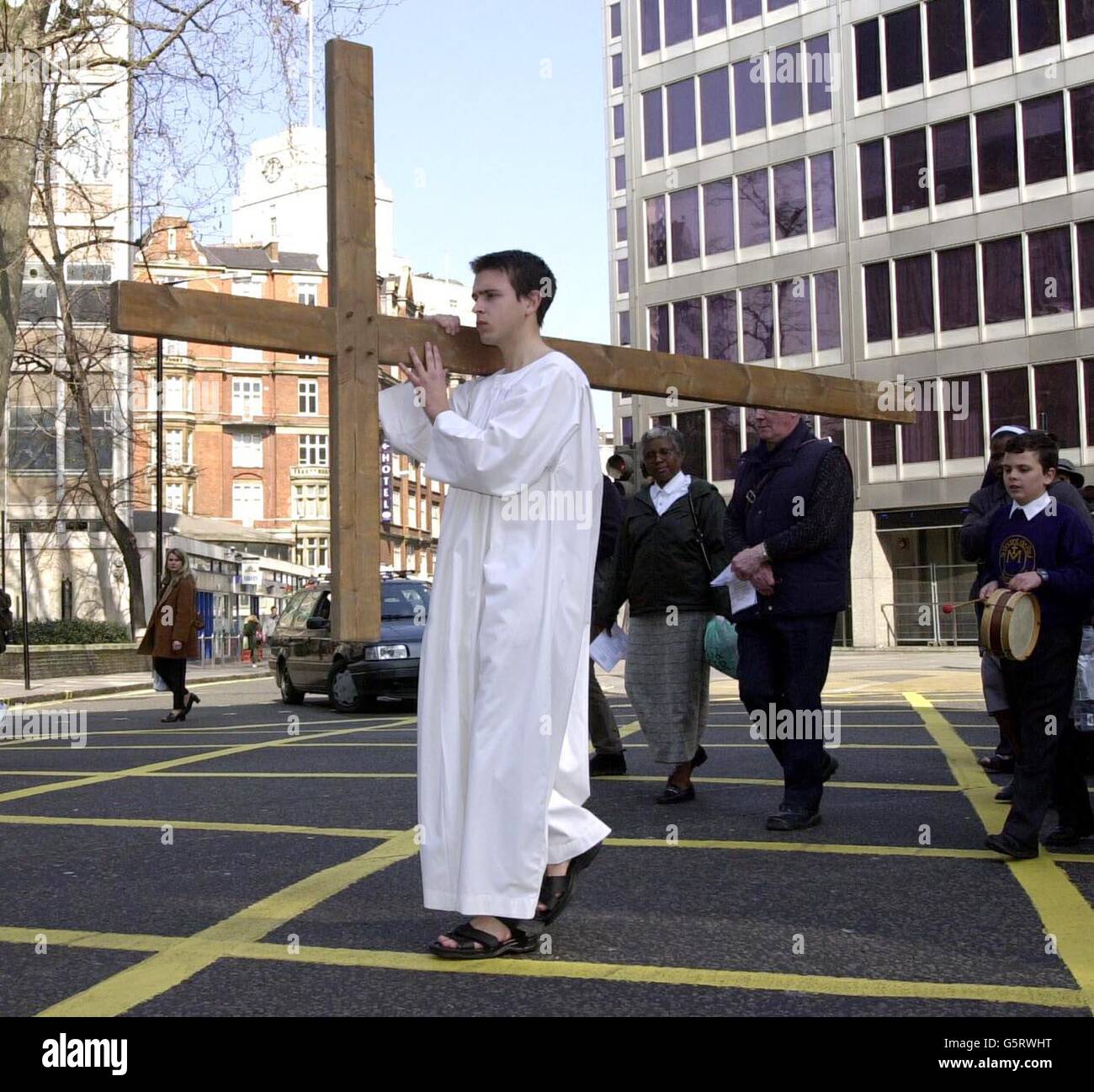 Il vicedirettore prefetto della Cardinal Vaughan Memorial School ben Goddard porta una grande croce durante la Crocifissione sulla cerimonia di Victoria Street a Londra. Goddard ha camminato dalla Sala Centrale Metodista alla Cattedrale di Westminster per segnare il Venerdì Santo, portando una croce. Foto Stock