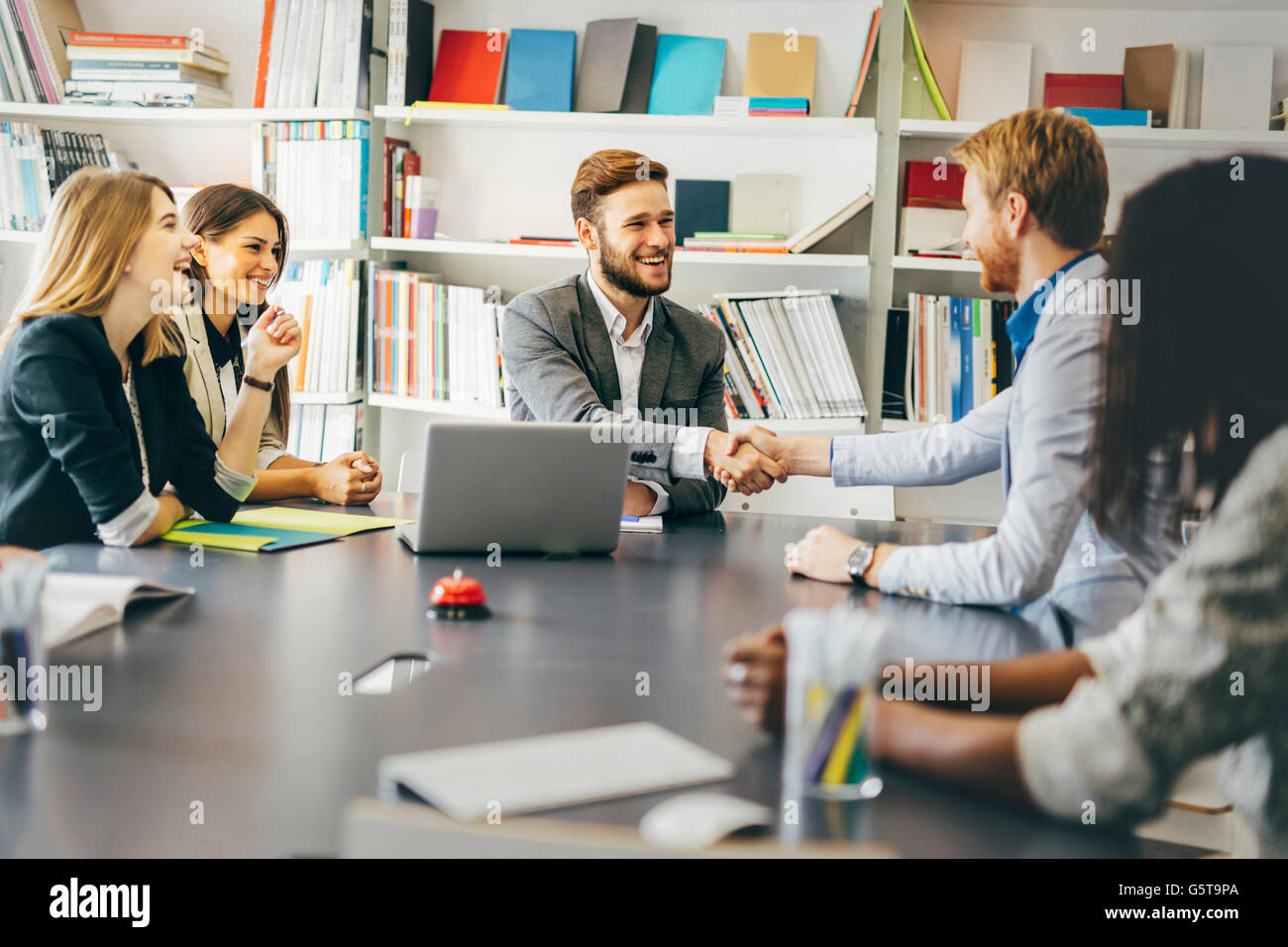 Gli imprenditori si stringono la mano in ufficio con i colleghi e lo staff di sedere a tavola con loro Foto Stock