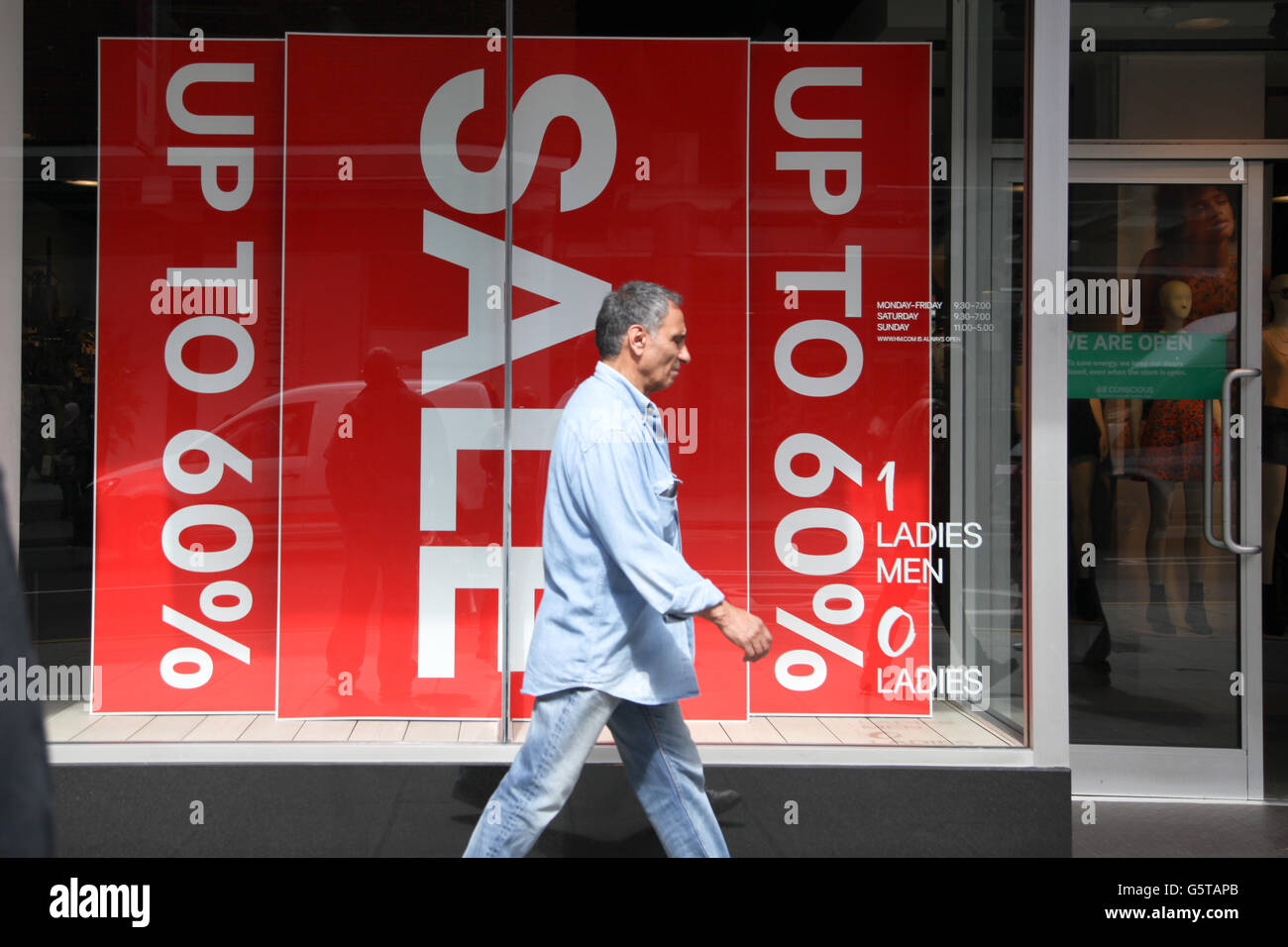 Una passeggiate passerby passato il segno di vendita in store H&M in legno verde, a nord di Londra. Foto Stock