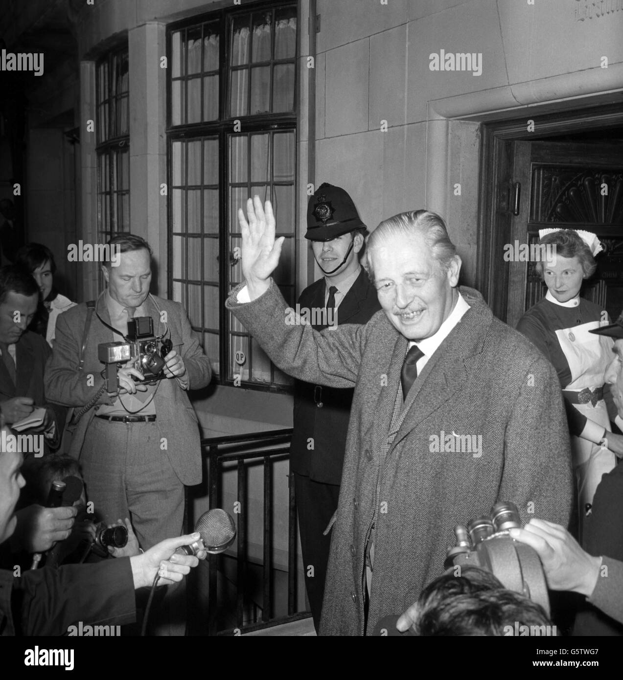 Harold Macmillan, l'ex primo ministro, ondeggia mentre lascia la macchina per arrivare al King Edward VII Hospital di Marylebone, Londra, dopo aver guidato con sua moglie, Lady Dorothy Macmillan. Al suo ritorno in ospedale, il signor Macmillan è stato portato all'interno di una sedia a rotelle. Sta recuperando da un'operazione della ghiandola prostatica. Foto Stock