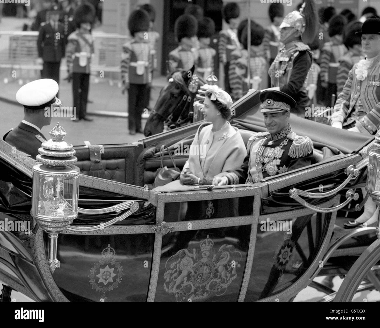 Lo Shah dell'Iran siede con la regina Elisabetta II in una carrozza aperta mentre guidano con il duca di Edimburgo a Buckingham Palace dalla stazione Victoria, Londra. Foto Stock