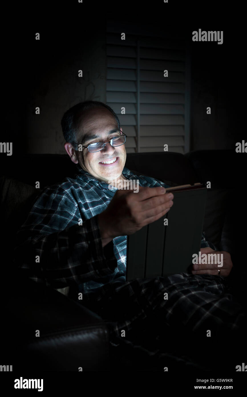 Uomo di mezza età indossando pigiami lettura compressa durante la notte nel letto cercando felice e sorridente Foto Stock