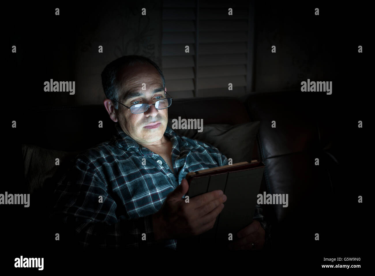 Uomo di mezza età in pigiama tablet di lettura di notte con espressione seria, spazio di copia Foto Stock
