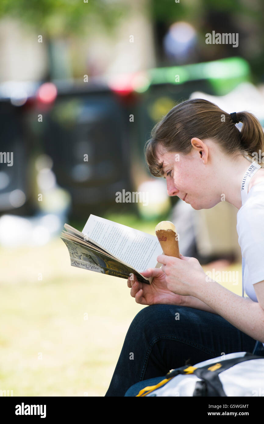 Una giovane donna godendo di mangiare un gelato e la lettura di un libro nel caldo sole estivo presso la Hay Festival della letteratura e delle arti, Hay on Wye, Powys, Wales UK, domenica 05 giugno 2016 Foto Stock