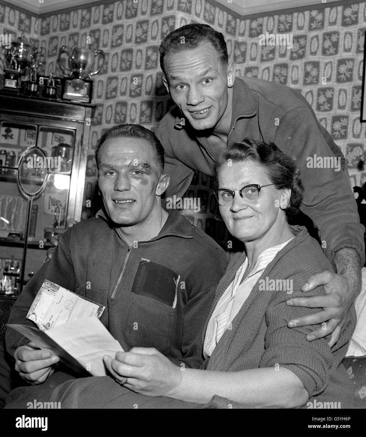 Henry Cooper, che ha sconvolto le classifiche mondiali americane con la sua grande vittoria sul banchiere dell'Arizona Zora Folley a Wembley, legge messaggi di congratulazioni alla sua Bellingham, Kent, casa. Con lui sono sua madre e suo fratello, George. Henry è ora ansioso di una partita con il campione del mondo Floyd Patterson. Foto Stock