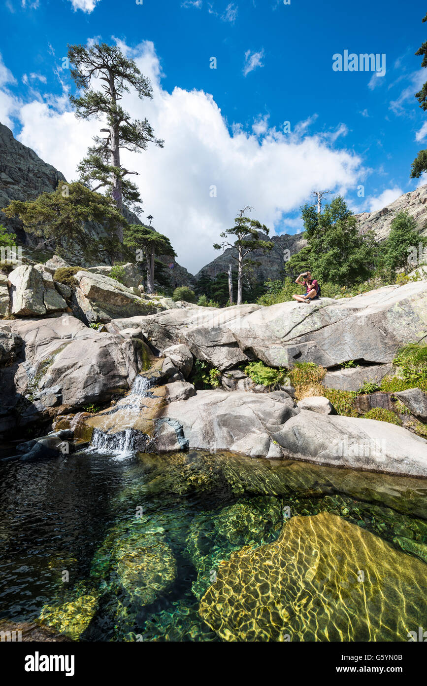 Giovane uomo seduto accanto ad una piscina con una piccola cascata in montagna, fiume Golo, Parco Naturale della Corsica Foto Stock