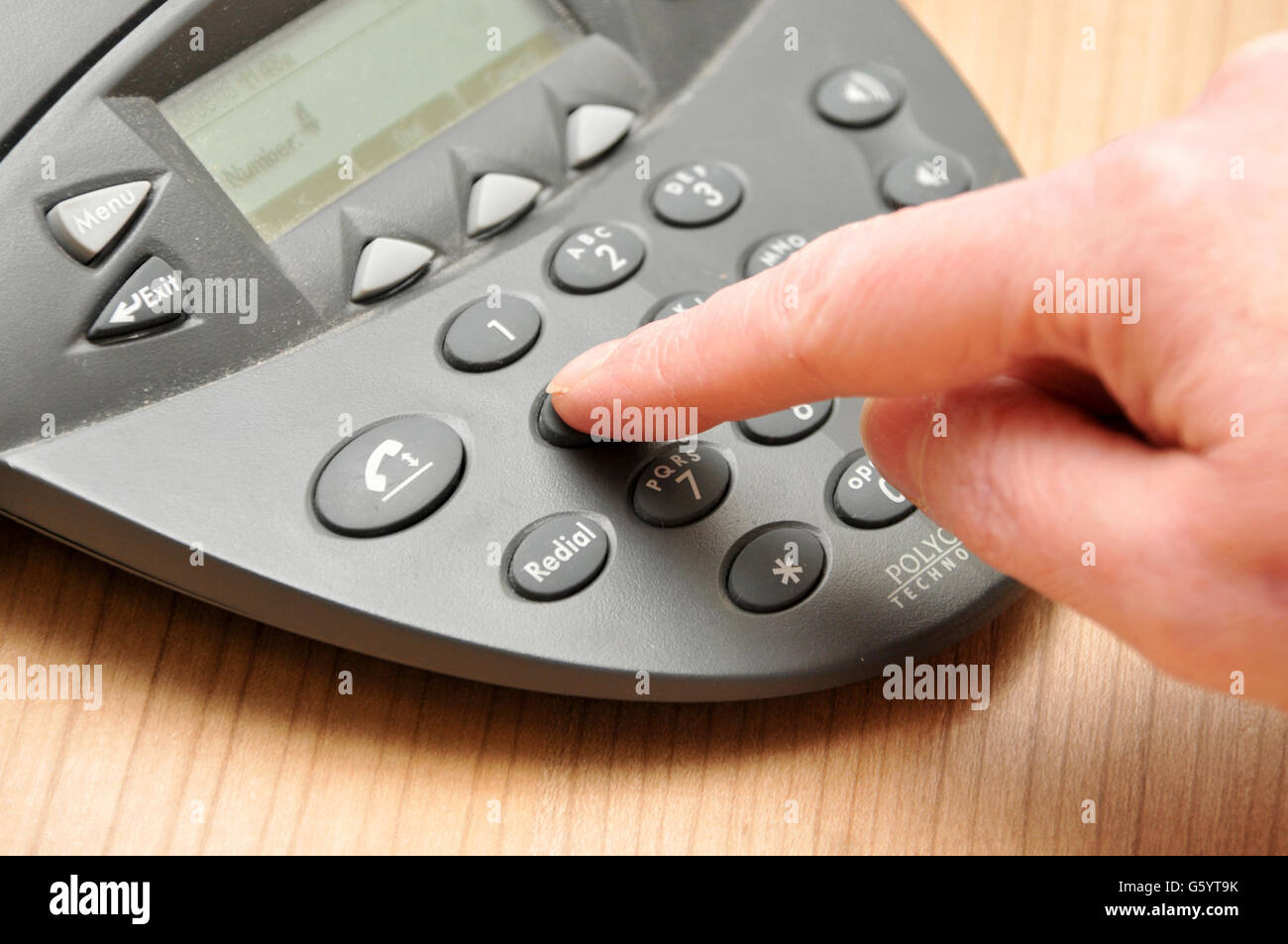 Azioni aziendali. Una dipendente femminile compone un numero di telefono su un telefono per una chiamata in conferenza durante una riunione Foto Stock
