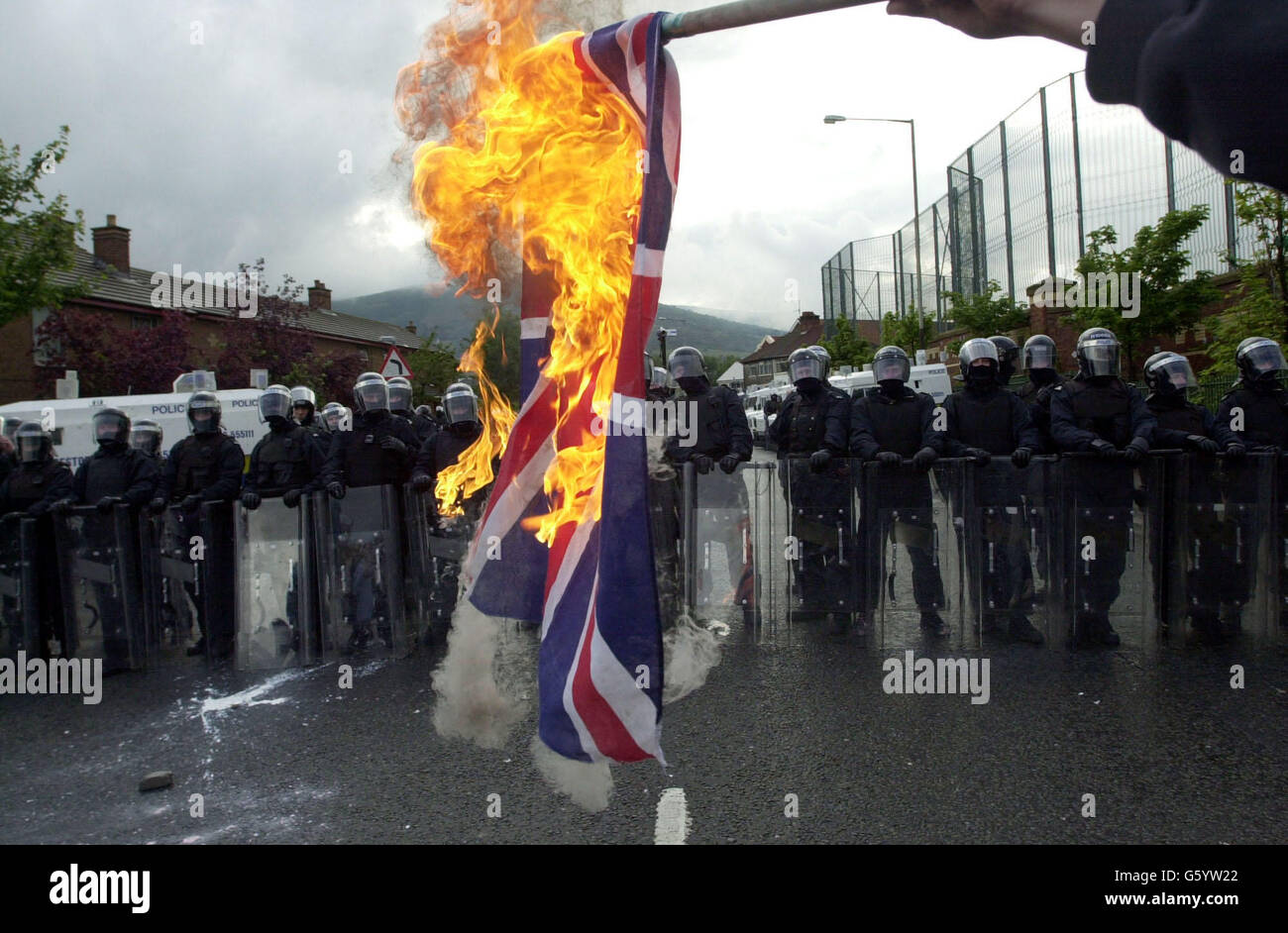 La polizia ha una linea, mentre i giovani cattolici bruciano una bandiera di Union Jack sulla Springfield Road, a ovest di Belfast. La polizia ha sofferto una sbarramento di bombe a benzina, fuochi d'artificio e mattoni dopo che gli ufficiali hanno sparato un bastone di plastica ai dimostranti che hanno attaccato una parata di ordine arancione in un'area nazionalista. I problemi sono iniziati quando i manifestanti cattolici hanno visto Orangemen salire su una parte contesa della Springfield Road. Foto Stock