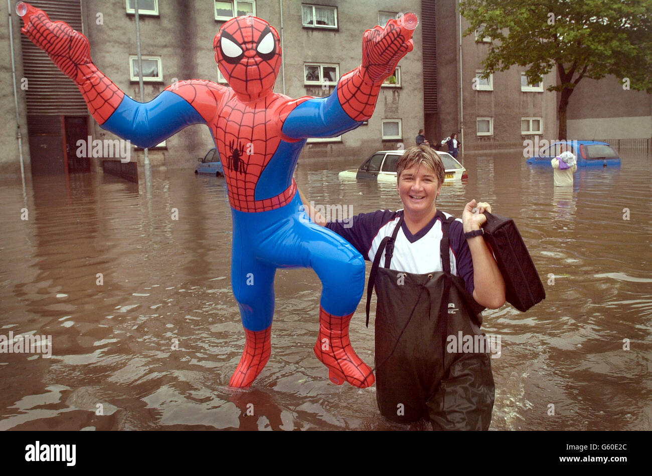 Resident Ally Allan non può fare a meno di ridere, in quanto porta una figura gonfiabile Spiderman, uno dei suoi molti possedimenti drappeggiati, dal suo flat allagato di fronte a un vicino di asciugare, in Cockenzie Street nella zona di Shettleston a Glasgow. *l'appartamento della signora Allan è stato sommerso in parecchi piedi d'acqua dopo le inondazioni di flash hanno causato la strada ad essere allagata in profondità di vita. Foto Stock