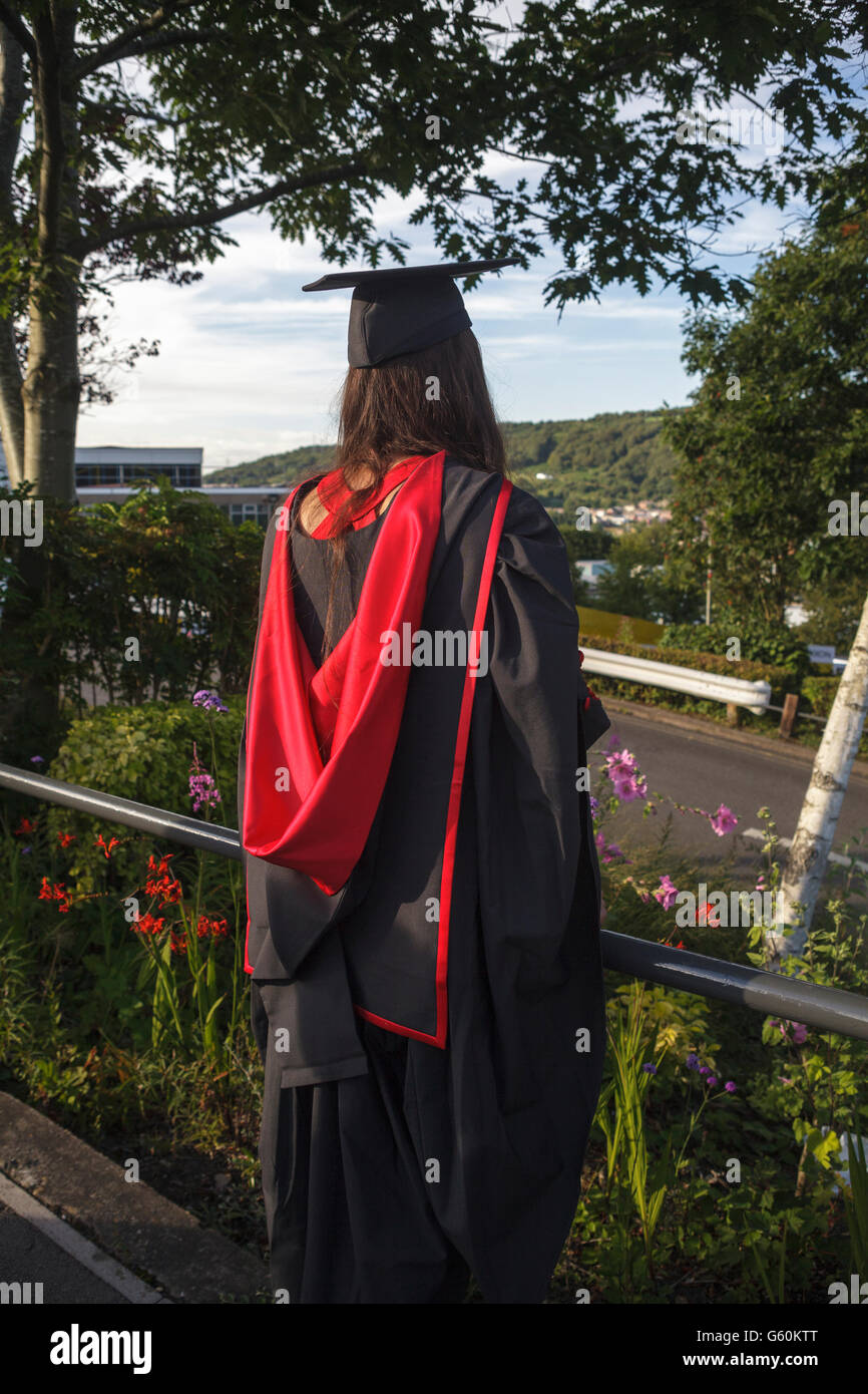 Lo studente che indossa un abito di laurea cercando in tutto il campus sul giorno di graduazione Foto Stock