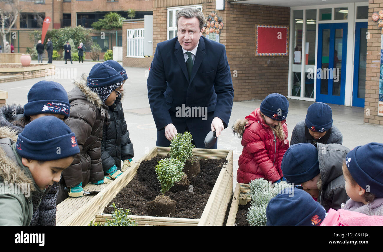 Il primo ministro David Cameron, al centro, aiuta i bambini delle scuole a piantare arbusti, durante una visita alla Ashburnham Community School a Londra ovest. Foto Stock