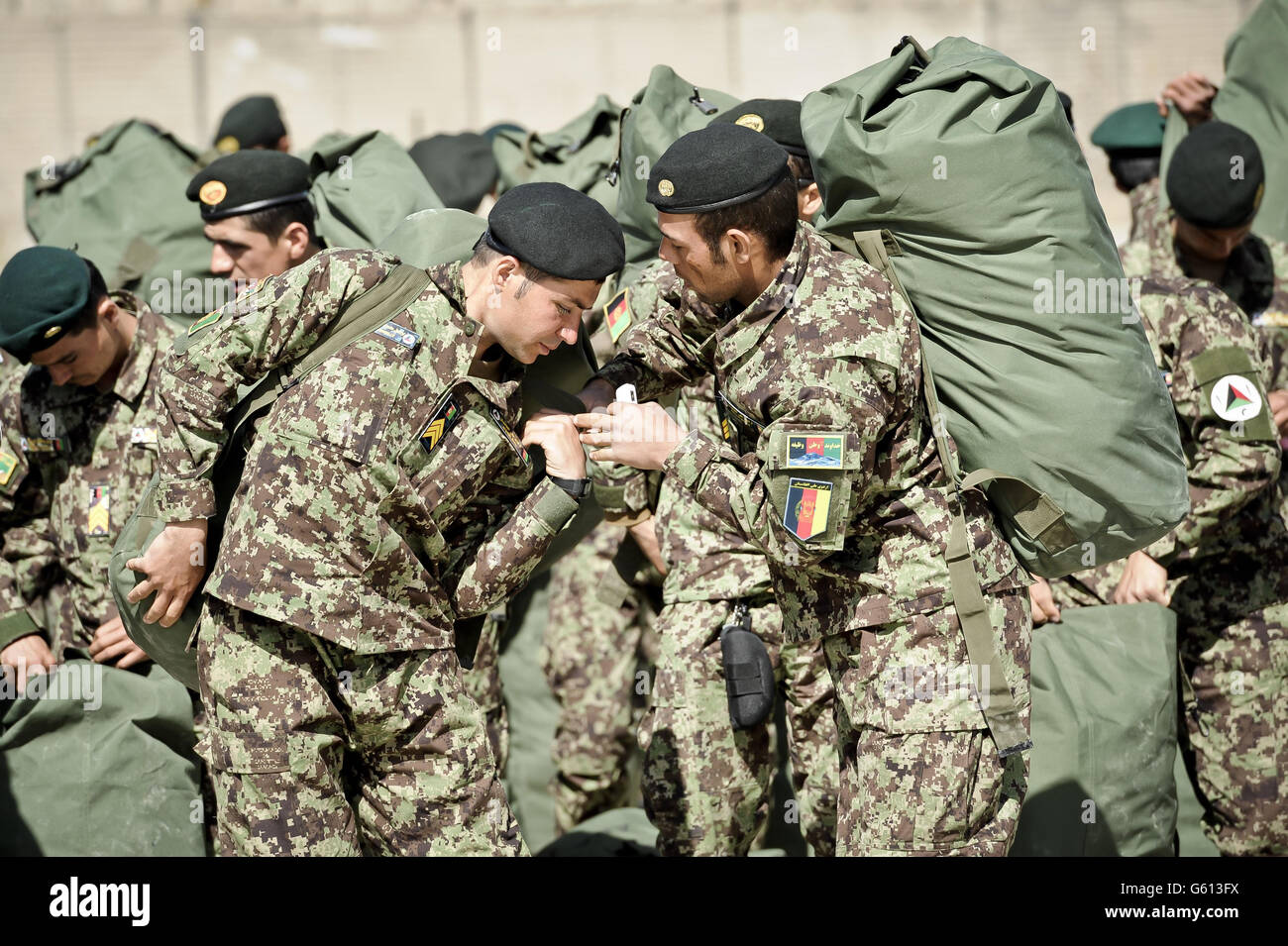 Gli ufficiali non commissionati dell'esercito nazionale afgano si aiutano a vicenda con le loro borse di kit, contenenti tutti i loro beni, nella piazza della parata del Centro militare di addestramento di Kabul, Kabul, Afghanistan, dopo essere stati assegnati ad un'unità di campo e infine si dirigono per essere dispiegati in teatro per combattere i talebani. Foto Stock