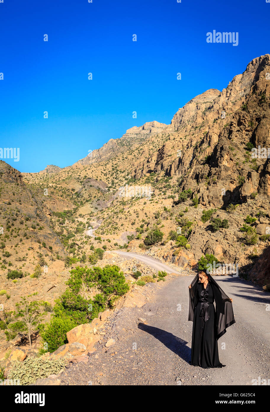 Una donna in nero abaya sta camminando su una strada in Al montagne Hajar in Oman Foto Stock