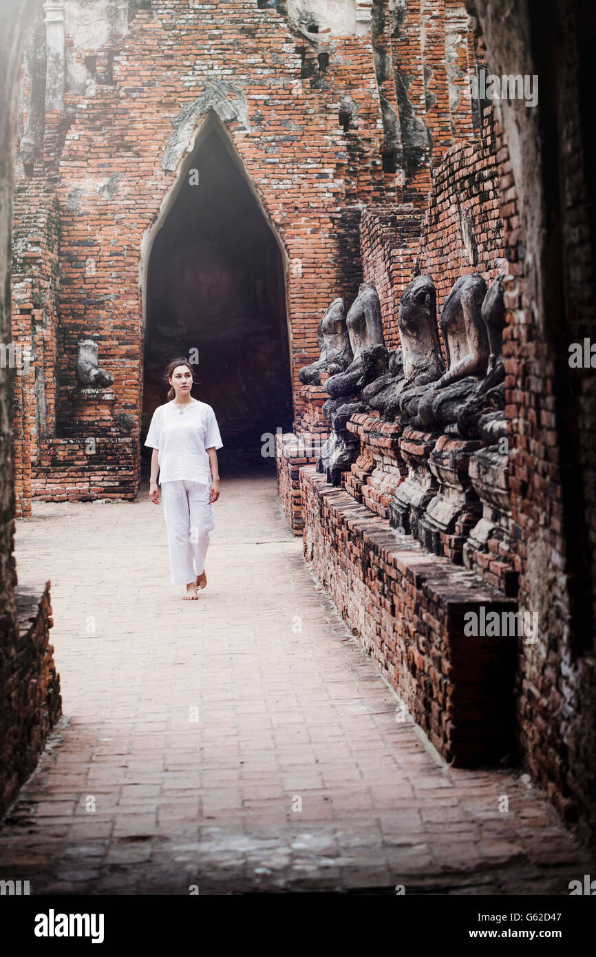 Una donna locale in bianco a piedi attraverso un tempio buddista in Ayutthaya sito Patrimonio Mondiale Foto Stock