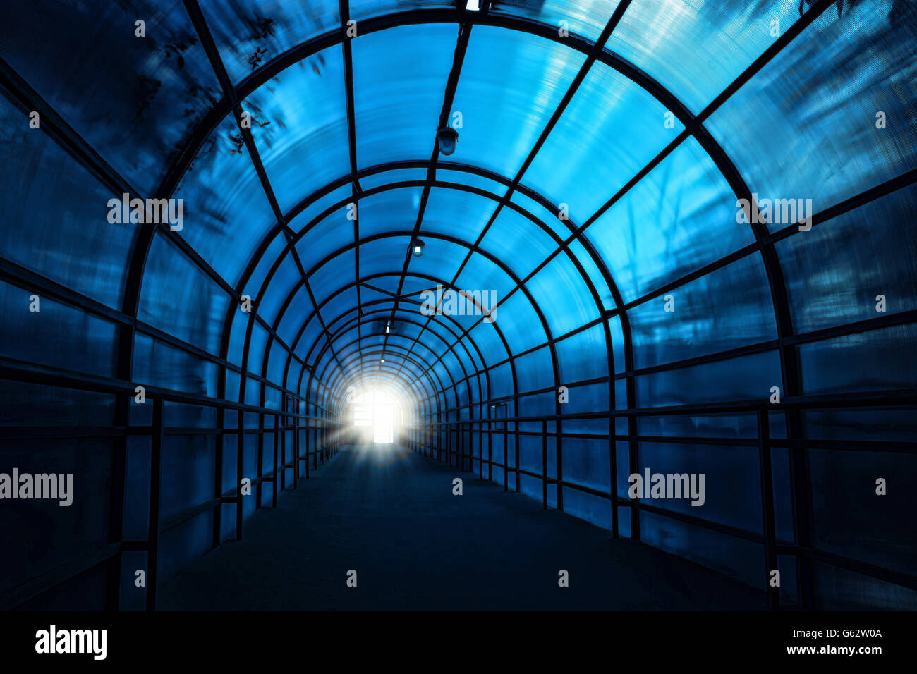 Blu scuro tunnel sinistre con ombre sui muri e la luce alla fine di esso Foto Stock