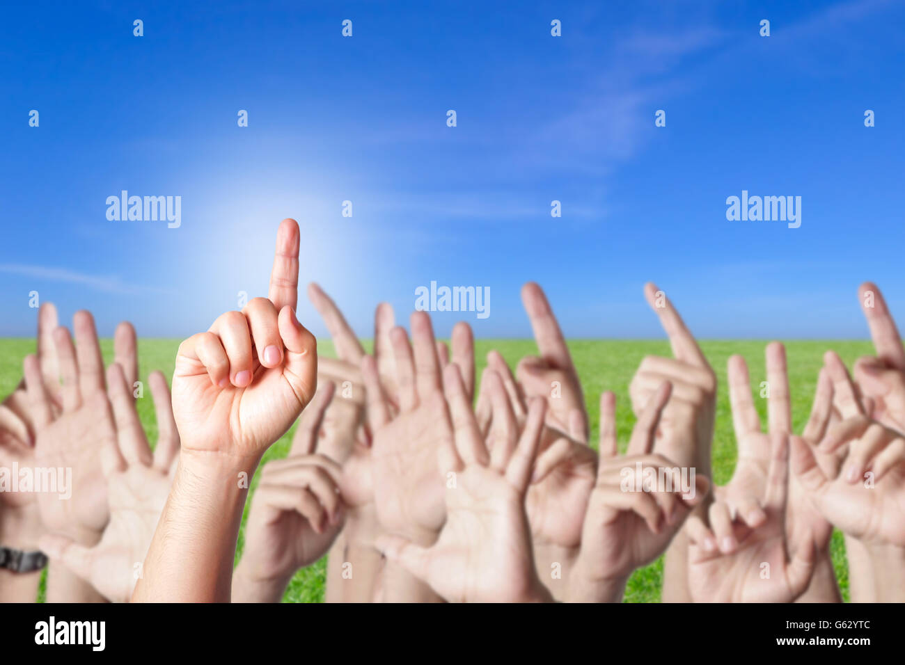 Gruppo di persone che allevano le mani per rispondere a una domanda su un campo verde con il blu del cielo Foto Stock