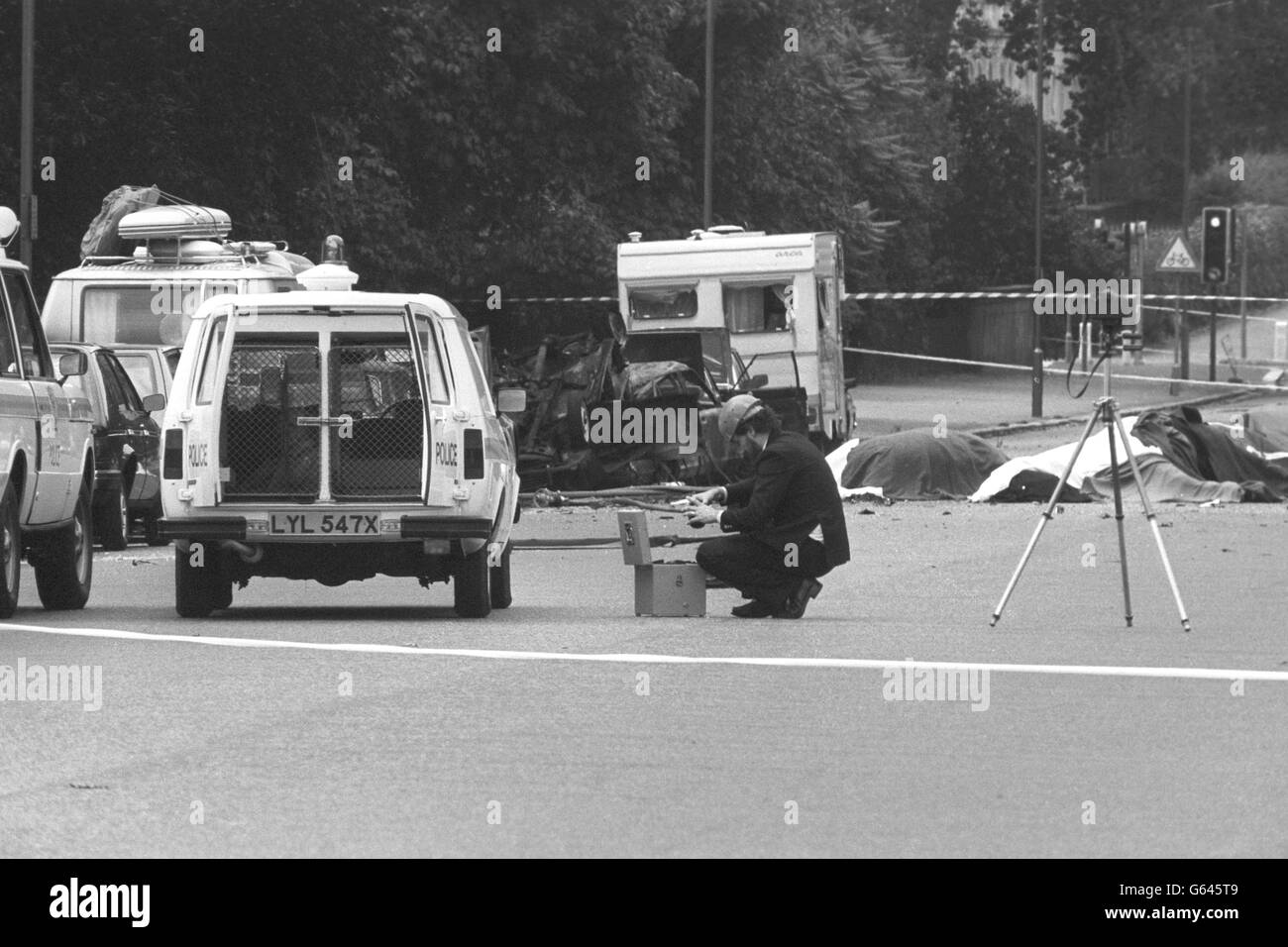 Un fotografo di polizia sulla scena dell'esplosione di oggi a Rotton Row, Londra, dopo una bomba è esploso vicino a una festa di cavalieri a Whitehall. Le auto distrutte sono sul lato della strada (a sinistra) e i cavalli distrutti dopo essere stati feriti nell'esplosione sono coperti da coperte. Foto Stock
