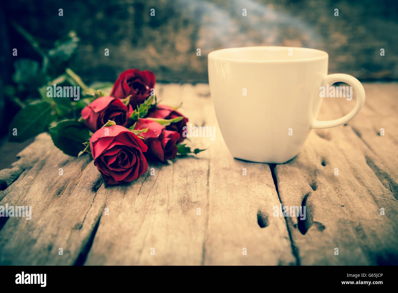 Bouquet di bellissime rose rosse e fumante tazza di caffè per il giorno di San Valentino sul sfocata sullo sfondo di legno. Vintage stile dell'immagine. Foto Stock