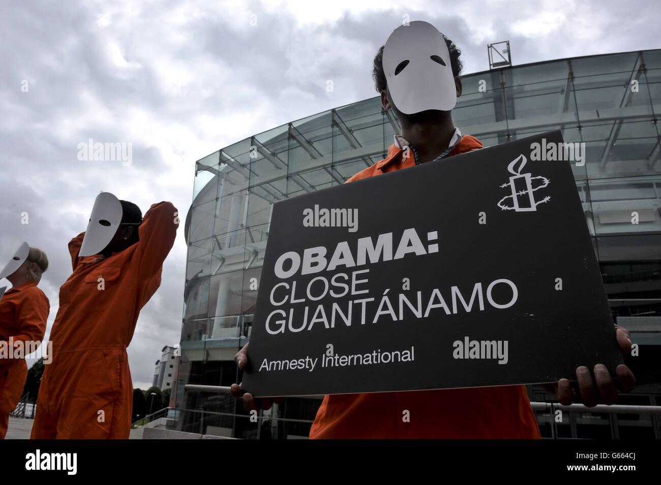 I manifestanti di Amnesty International vestiti di tute e maschere di salto arancioni, tengono cartelli chiedendo che il presidente degli Stati Uniti, Barack Obama, chiuda Guantanamo, mentre si riuniscono fuori dal Waterfront, Belfast, in vista del vertice del G8. Foto Stock