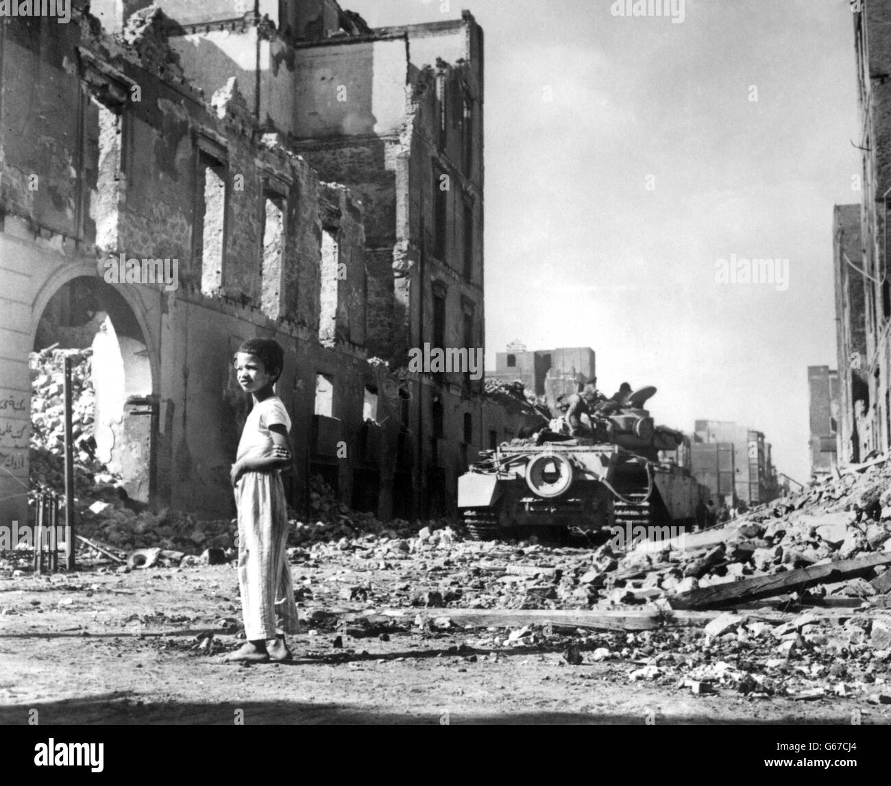 Un ragazzo egiziano fa un'indagine sulla devastazione mentre un carro armato britannico si muove attraverso una strada in rovina a Port Said, ora occupato dalle truppe anglo-francesi in attesa della forza di polizia delle Nazioni Unite Foto Stock