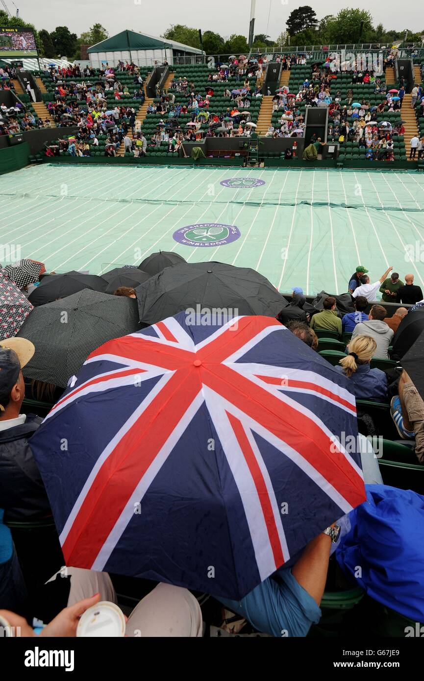 I tifosi si riparano dalla pioggia sul campo due durante il quarto giorno dei Campionati di Wimbledon all'All England Lawn Tennis and Croquet Club, Wimbledon. Foto Stock