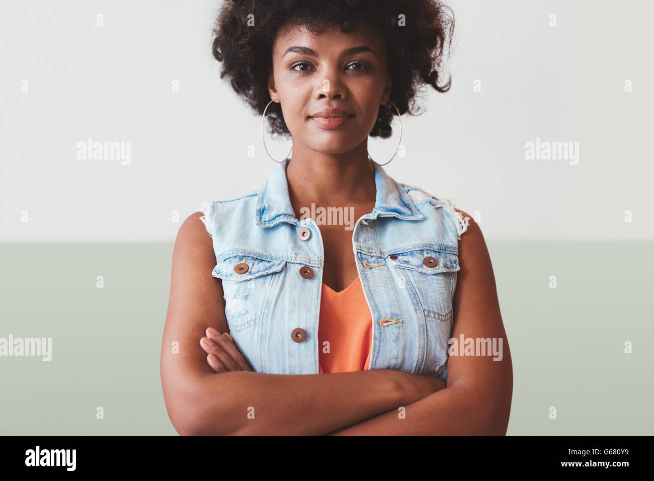 Ritratto di giovane e bella donna in piedi con le braccia incrociate contro una parete. Fiducioso giovane africano modello femminile in smart c Foto Stock