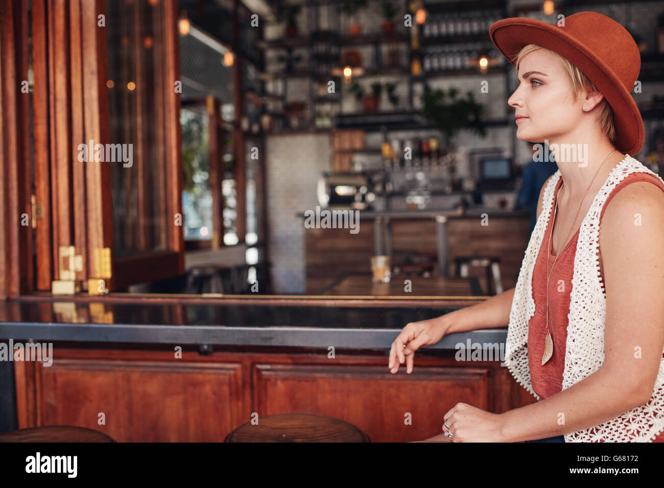Vista laterale della bellissima giovane donna caucasica seduti al bancone e guardando lontano. Indossa hat in attesa di qualcuno. Foto Stock