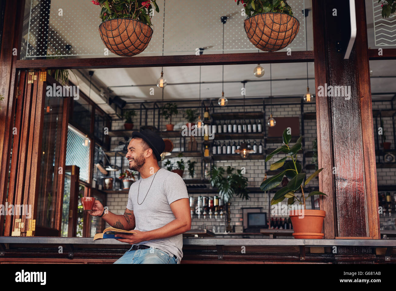 Felice giovane uomo a bere caffè e la lettura di libro in un bar. Giovane ragazzo gustando una tazza di caffè durante la lettura di un romanzo. Foto Stock