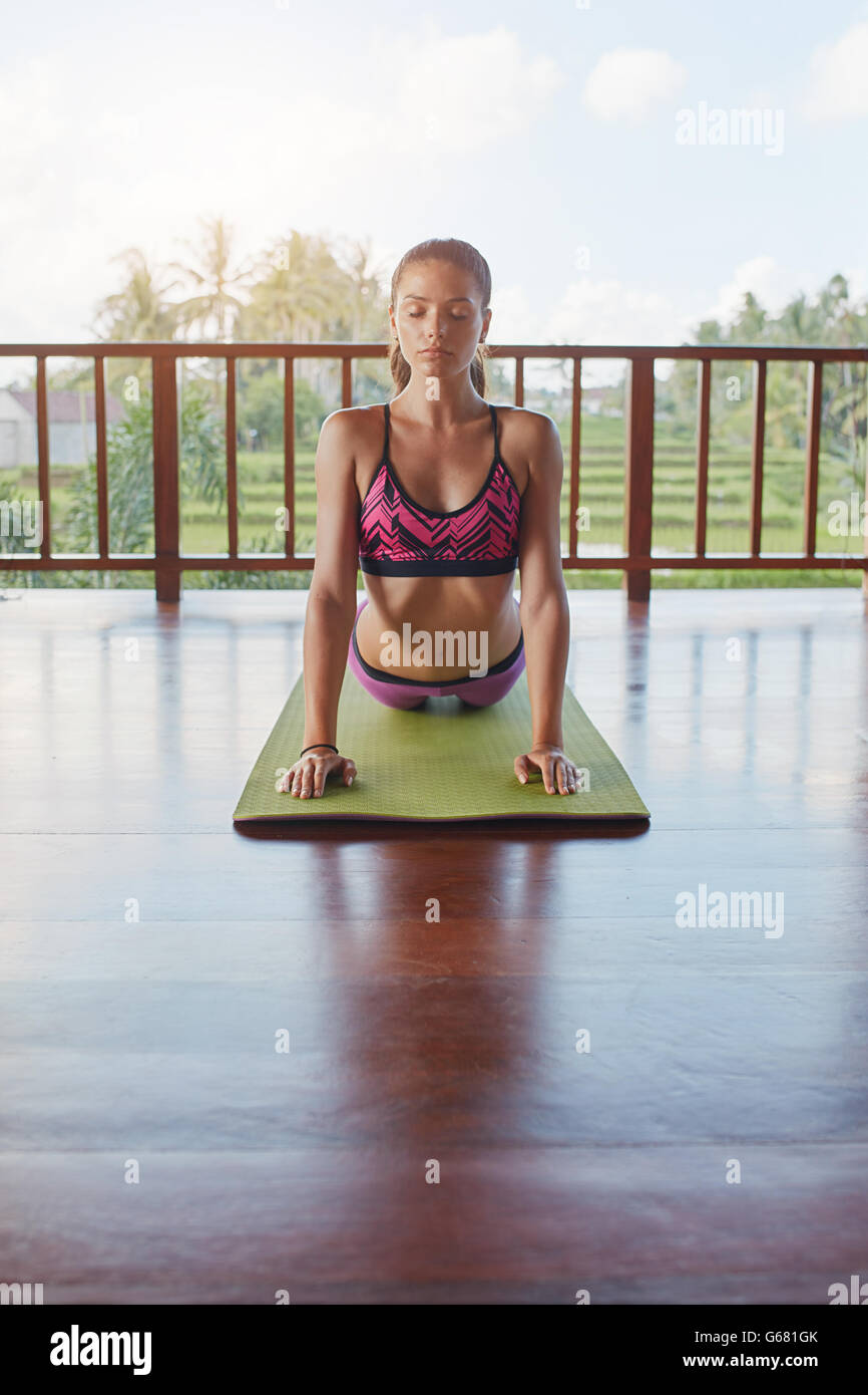 Colpo di giovane donna facendo cobra pone sul tappeto di esercizio in corso di yoga. Femmina Fitness facendo core tratto sul materassino yoga. Foto Stock