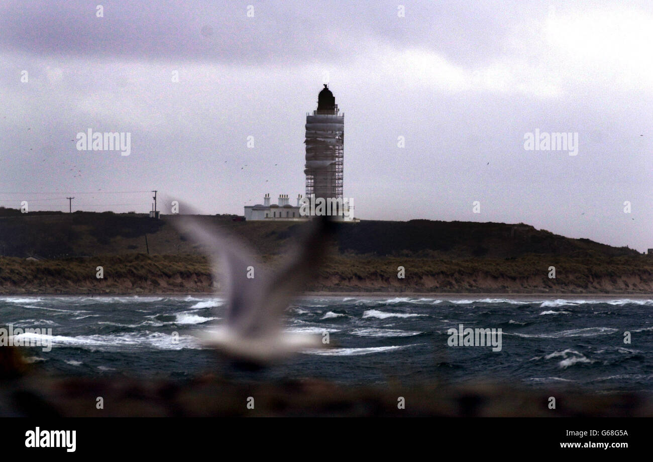 Un gabbiano lotta nel vento sulla spiaggia di Lossiemouth con il faro di Covesea sullo sfondo, Lossiemouth. Foto Stock