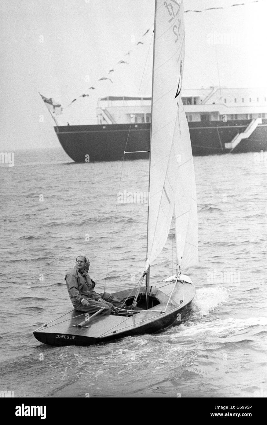 Con il Royal Yacht, Britannia sullo sfondo, il Principe Filippo, il Duca di Edimburgo e Yachtsman, Uffa Fox (nascosto dal Duca), sono mostrati a bordo della prima barca Coweslip Off Cowes, Isola di Wight, prima che Coweslip gareggesse nell'evento Flying quindici. Foto Stock