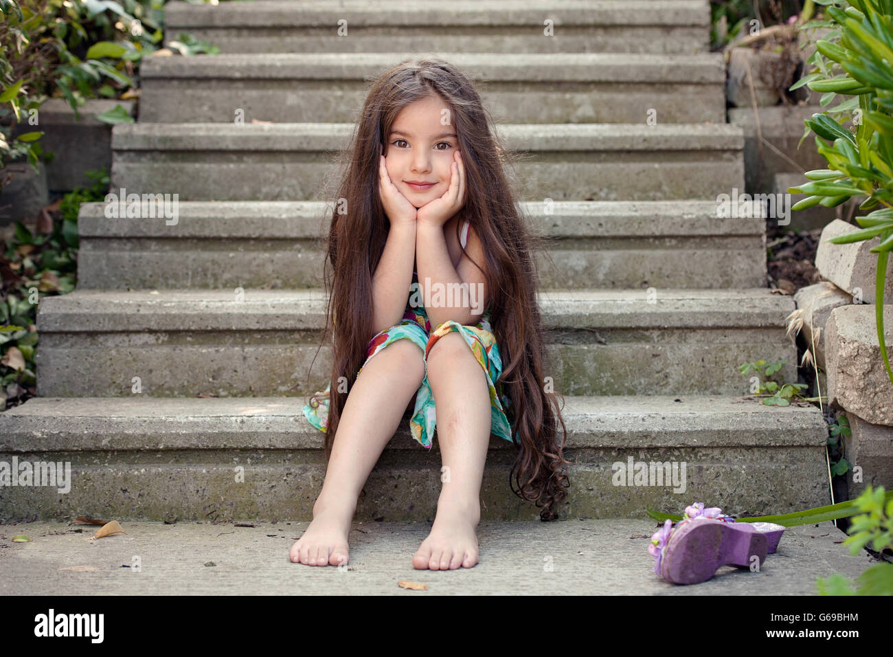 Piccola ragazza con i capelli lunghi seduto sui gradini Foto Stock