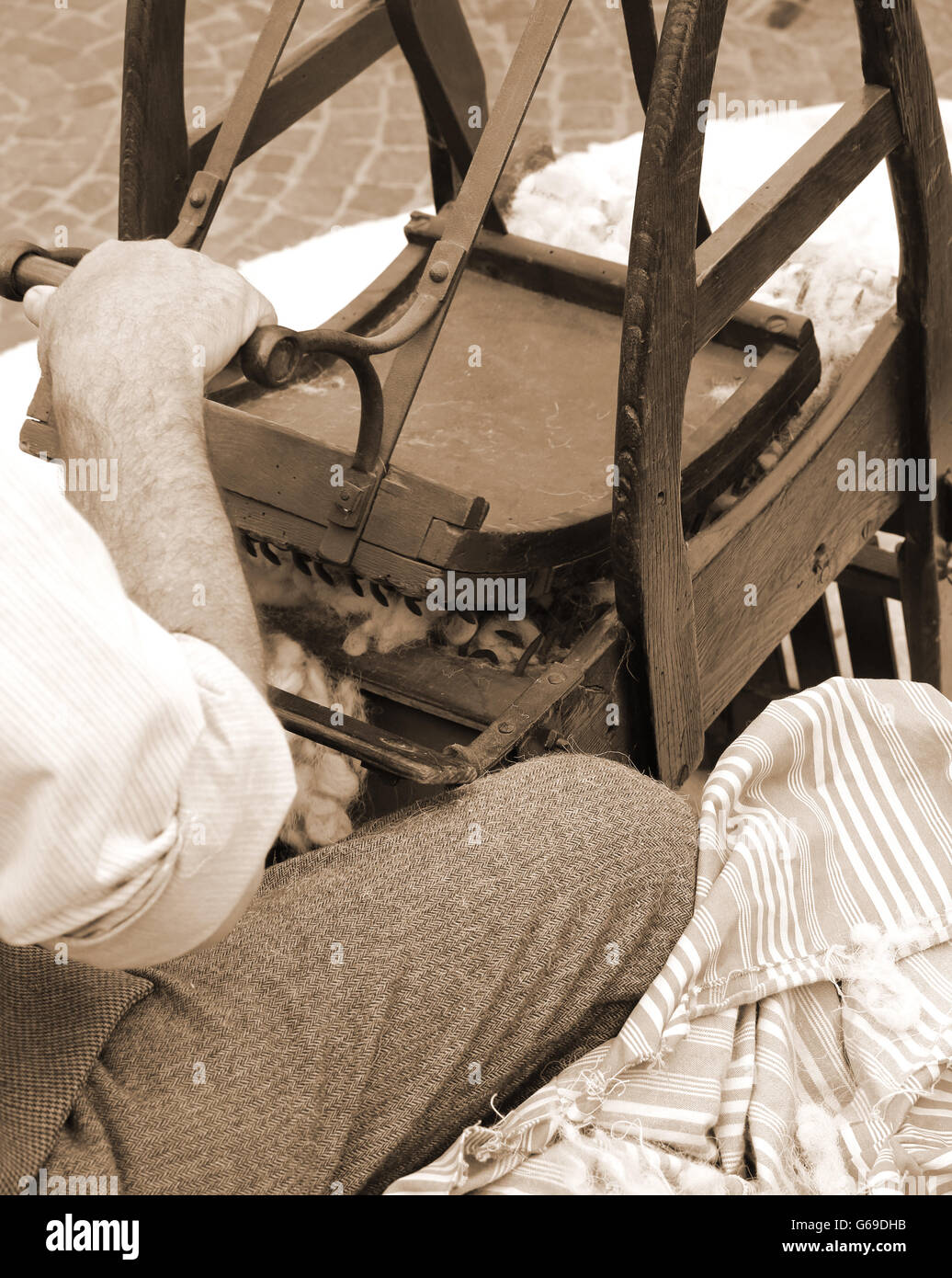 Carda Senior uomo mentre la cardatura lana o cotone con la vecchia macchina in legno Foto Stock