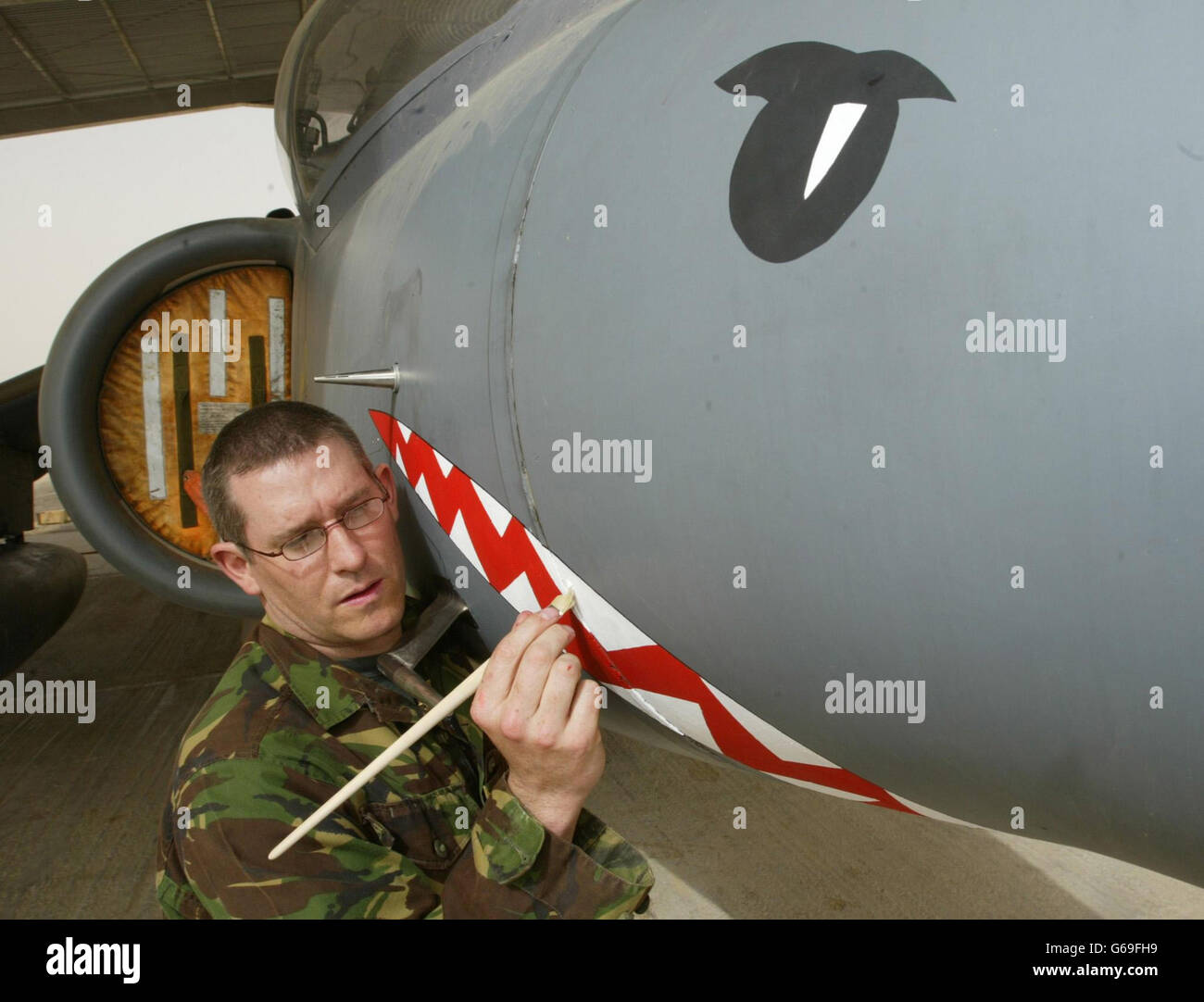 La bacca Adrian CPL dipinge i denti e gli occhi degli squali su un Harrier GR7 della British Royal Air Force, in quanto il maltempo impedisce di volare dalla loro base in Kuwait. * questa è la prima volta che un Harrier britannico GR7 è stato dipinto in questo modo, con l'aereo che è stato decorato solo come questo durante i periodi di conflitto reale. Foto Stock
