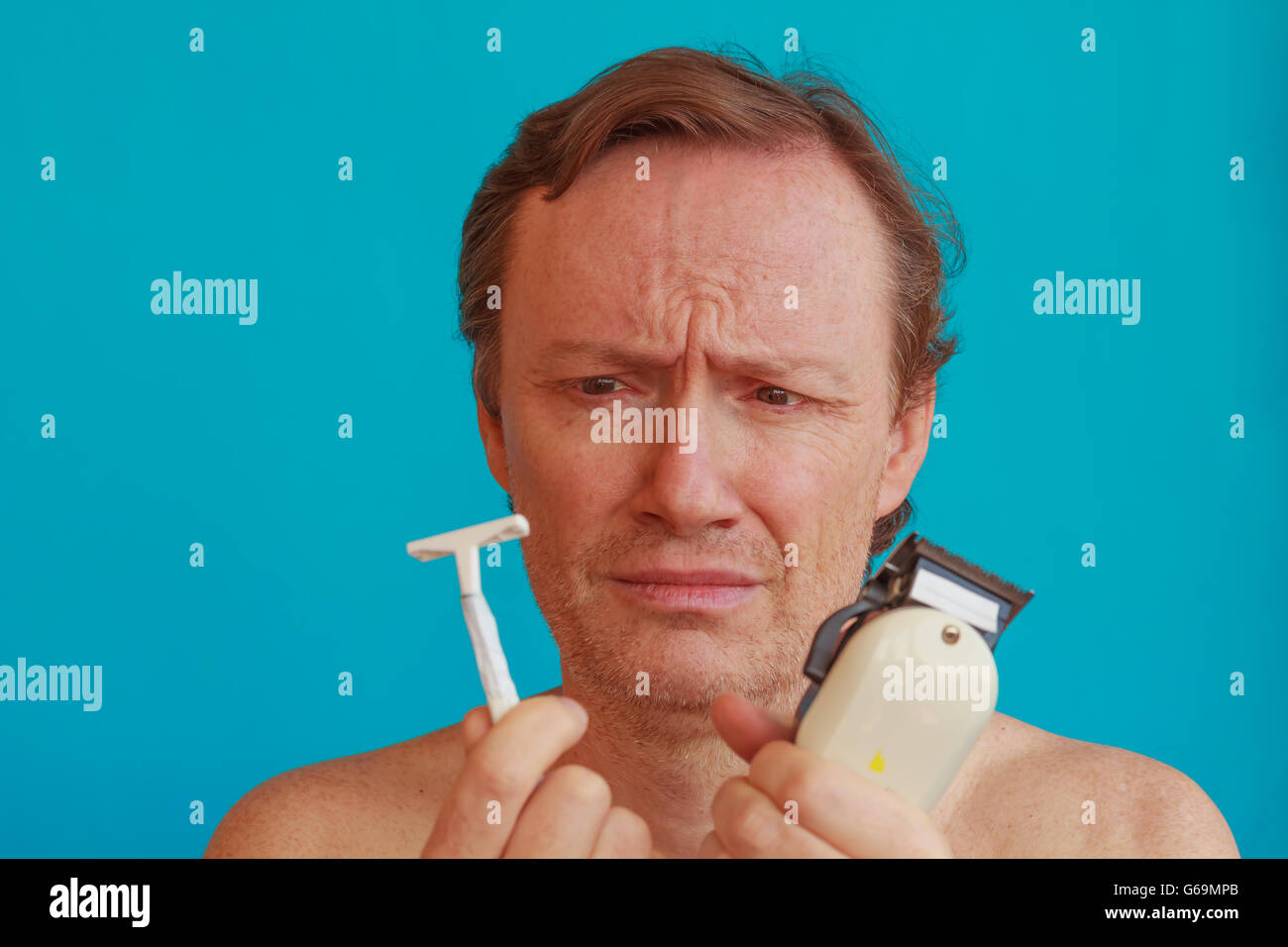 Un uomo per la rasatura ma è indeciso se scegliere il rasoio o un rasoio a lama Foto Stock