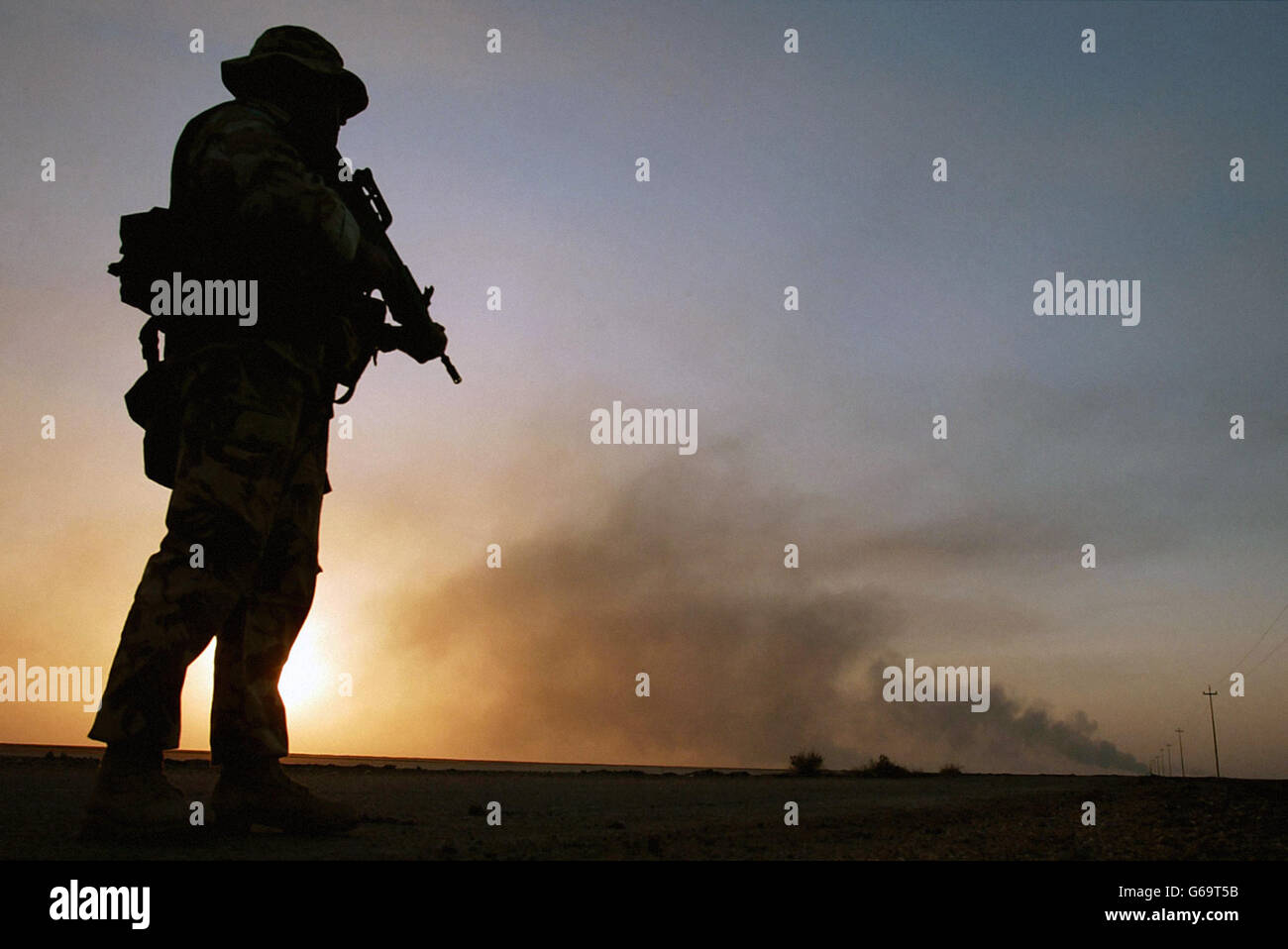 Un soldato britannico del 29 Commando Regiment Royal Artillery è in servizio come un incendio di petrolio brucia all'orizzonte nel sud dell'Iraq. Mentre il conflitto iracheno entra nella sua seconda settimana. Foto Stock
